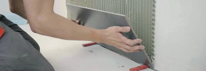 Person bringt Fliese an Wand an